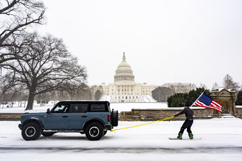 WASHINGTON, DC - JANUARY 25: Collin Sabine, from Washington, DC rides a snowboard holding an American flag while being pulled on the West Front of the US Capitol on January 25, 2026 in Washington, DC. A massive winter storm is expected to bring frigid temperatures, ice, and snow to millions of Americans across the nation. (Photo by Al Drago/Getty Images)