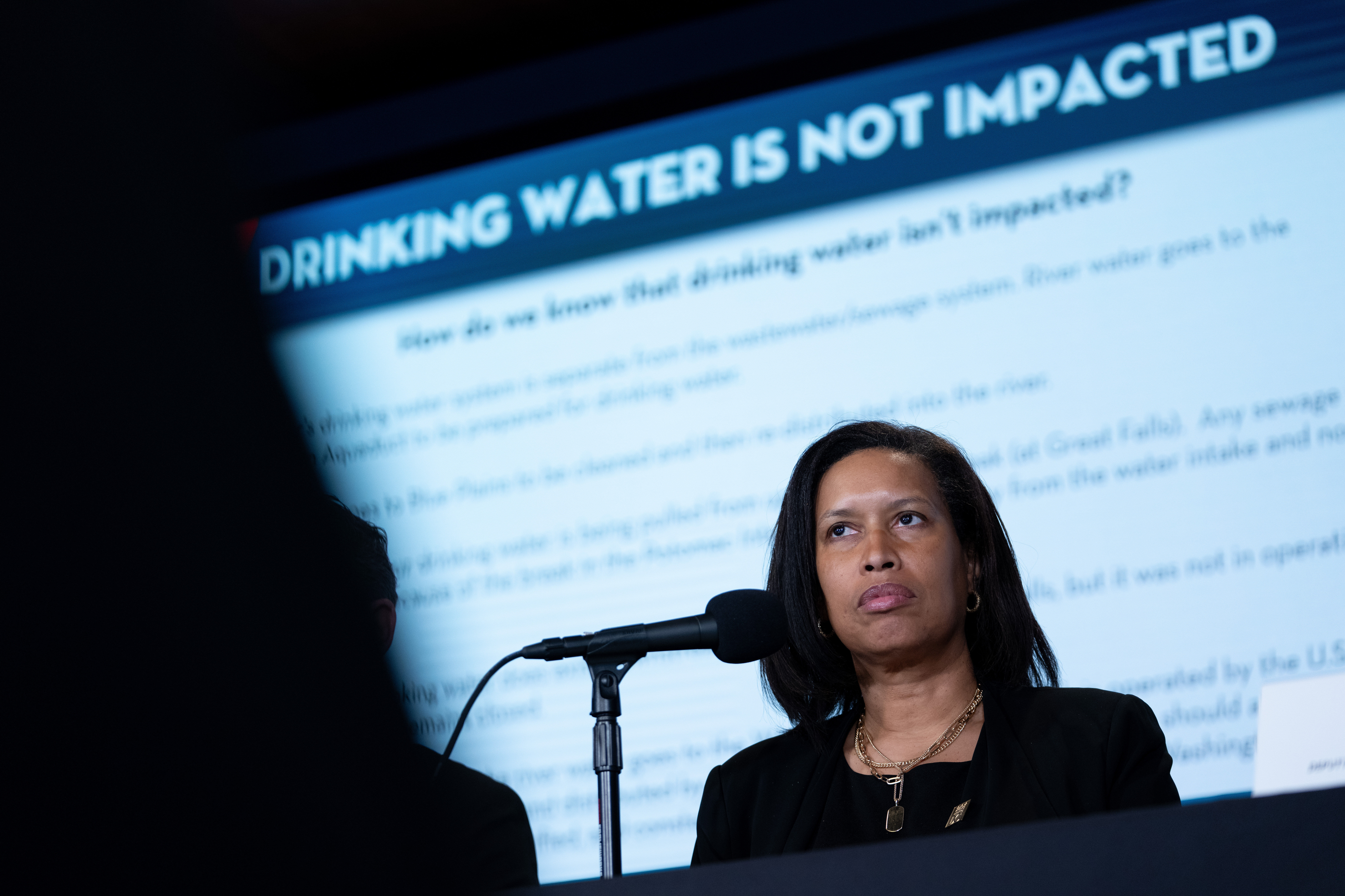 shot of woman sitting during news conference with microphone in face and slide projection behind her